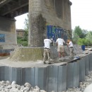 Photo de trois techniciens uretek réalisant des injections de résine expansive dans le sol sous un pont routier pour le stabiliser